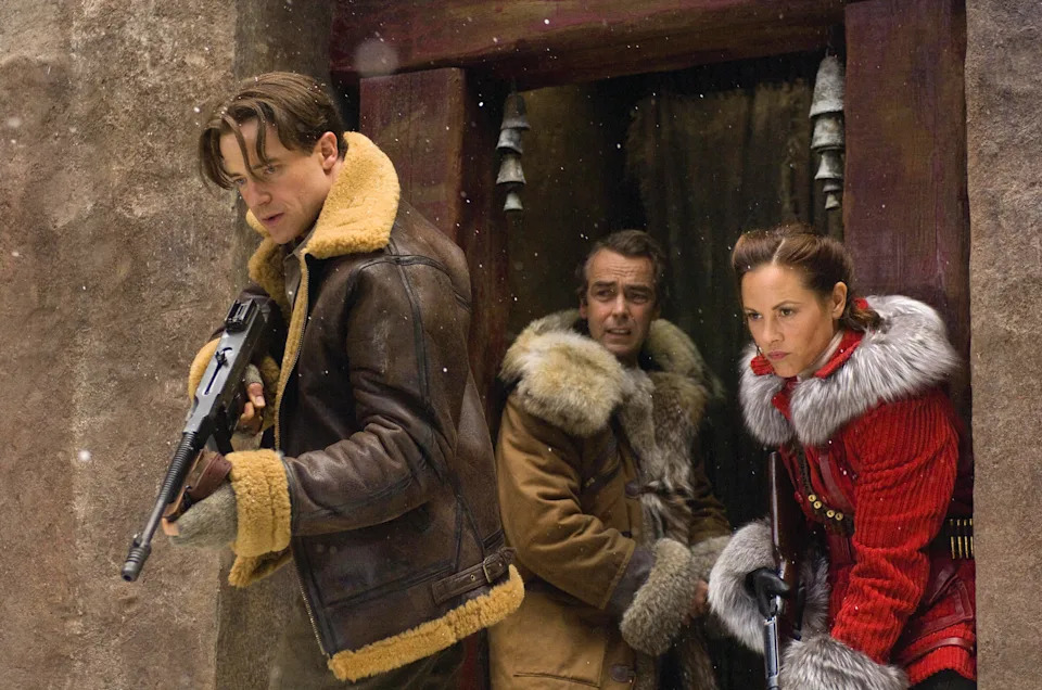 Three people in winter gear stand in a snowy doorway, holding weapons and looking alert