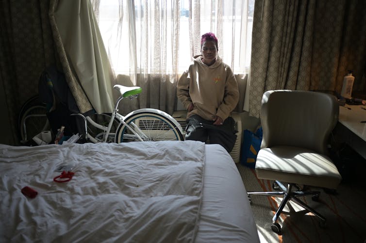 A woman sits in front of a hotel window next to a bike.