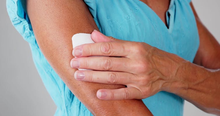 Woman putting an HRT patch on her upper arm.