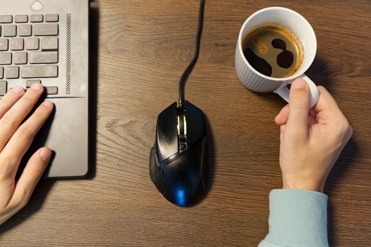 One hand on a keyboard, the other on a mug of coffee.