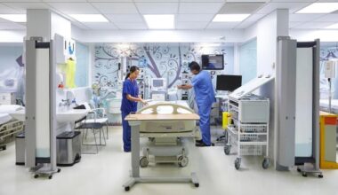 Two healthcare workers in blue scrubs prepare a hospital bed in a modern, well-equipped private ward.