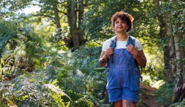 woman wearing denim short dungarees and a white tshirt walking in a forest setting.
