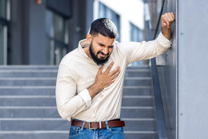 Man clutching chest in pain outdoors, illustrating patients brushing off terrifying symptoms as normal to doctors.