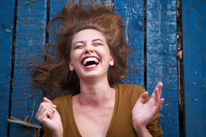 Young woman laughing joyfully, lying on blue wooden floor, illustrating patients brushing off terrifying symptoms as normal.