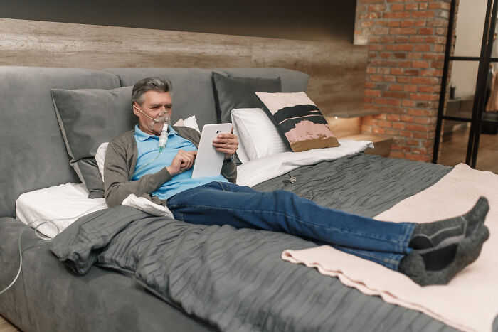 Older man using oxygen therapy at home resting in bed while reading on a digital tablet showing patients brushing off terrifying symptoms