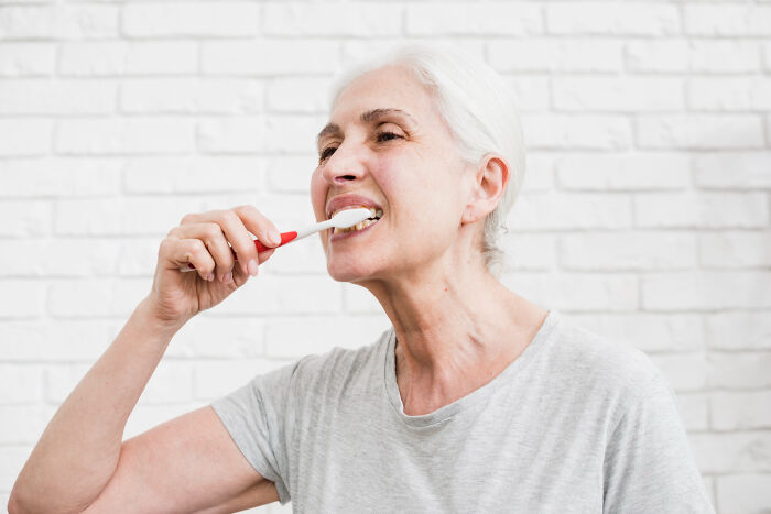 Elderly woman brushing teeth, illustrating patients brushing off terrifying symptoms considered normal by doctors.
