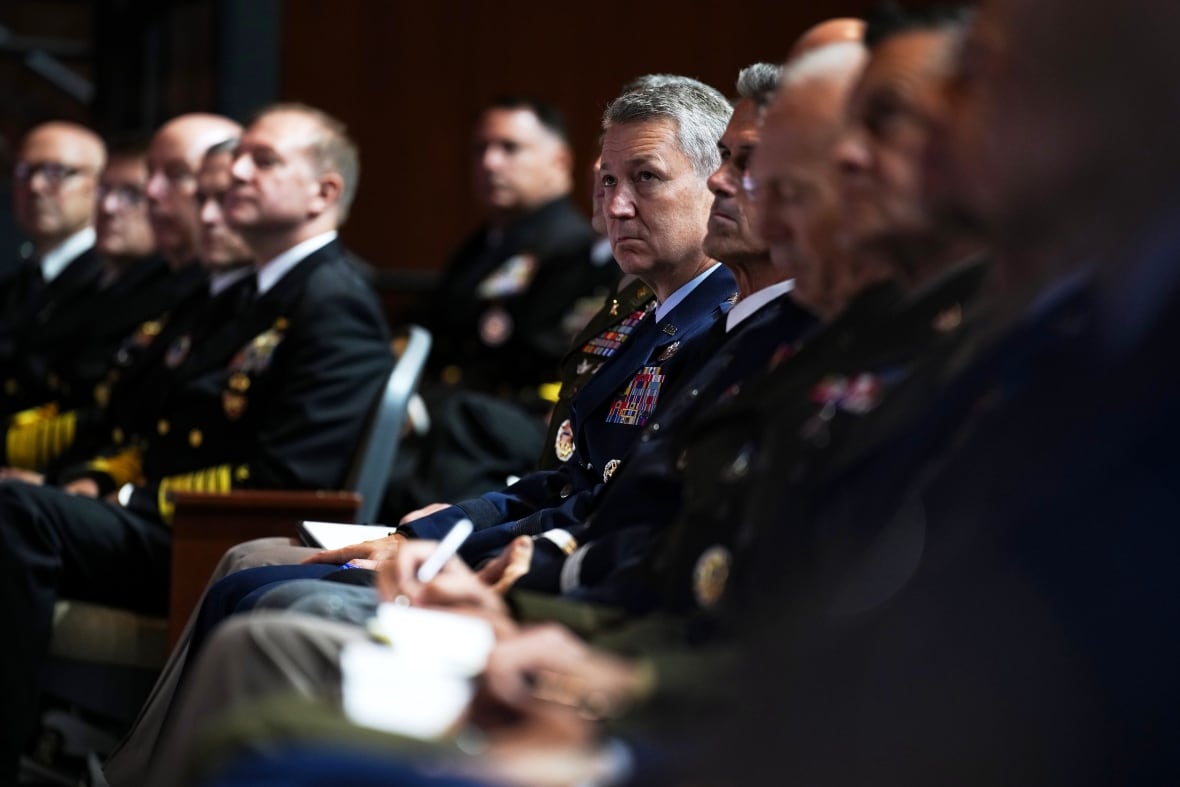 Men in military uniforms sit in an audience