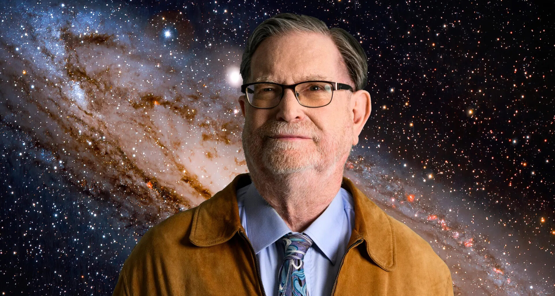a man in a brown leather jacket, blue shirt and glasses, with the Andromeda Galaxy in the background.