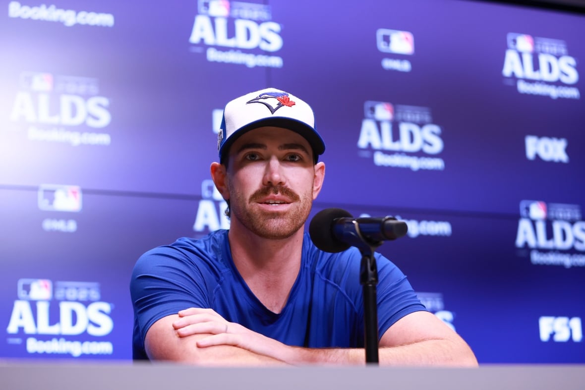A man with a moustache, sitting at a table, with his arms crossed.