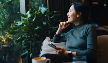 Woman smiling, holding phone and looking out of the window in a cafe, sitting on sofa after doing brain health exercises