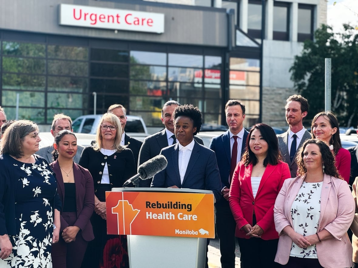 A person wearing a blazer stands at a podium in front a group of people.