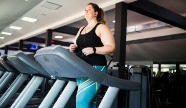 woman walking on a treadmill with earphones in, she's in a gym setting wearing turquoise leggings and black vest.