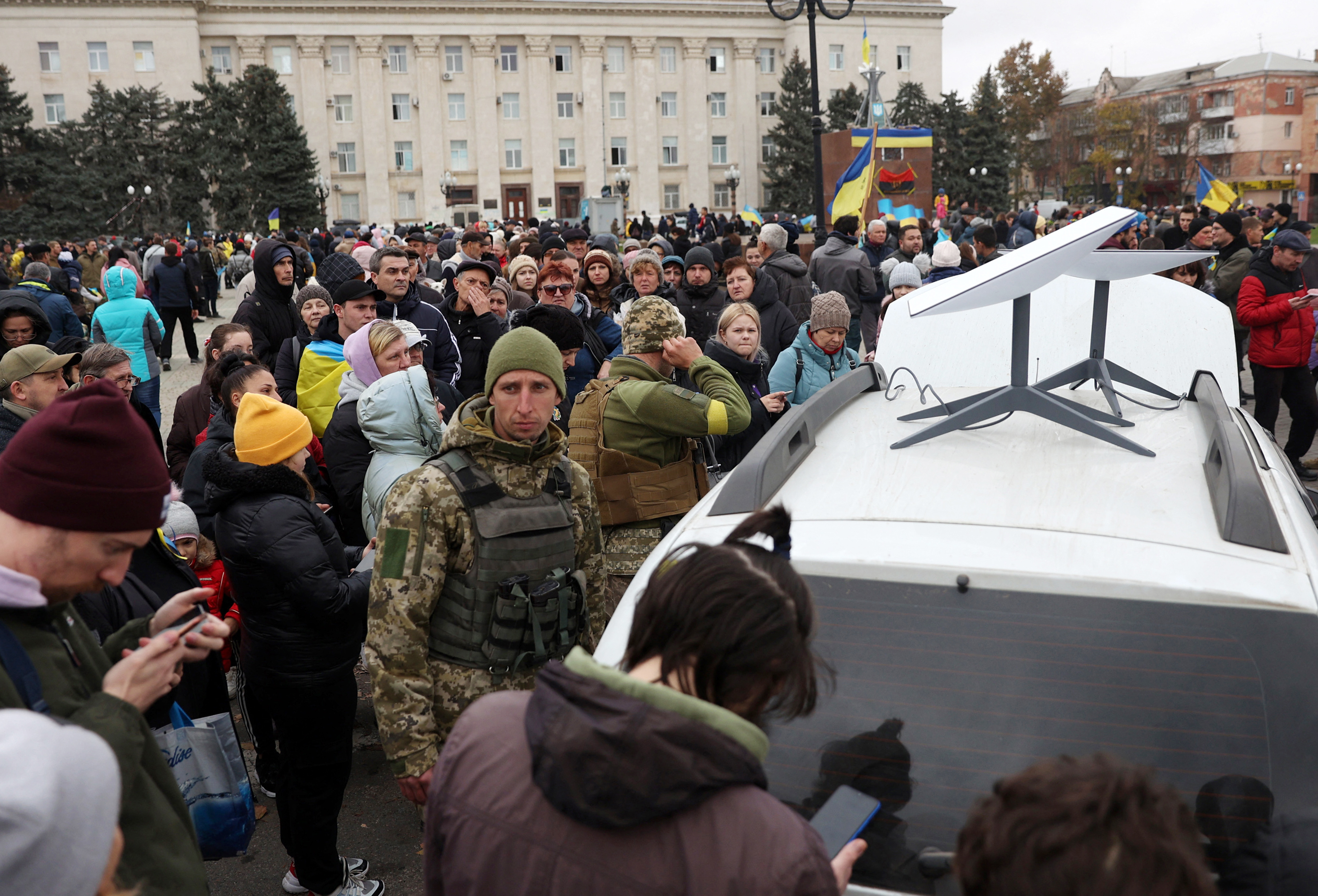 People in Kherson use their mobile phones near a Starlink satellite-based broadband station on a white car.