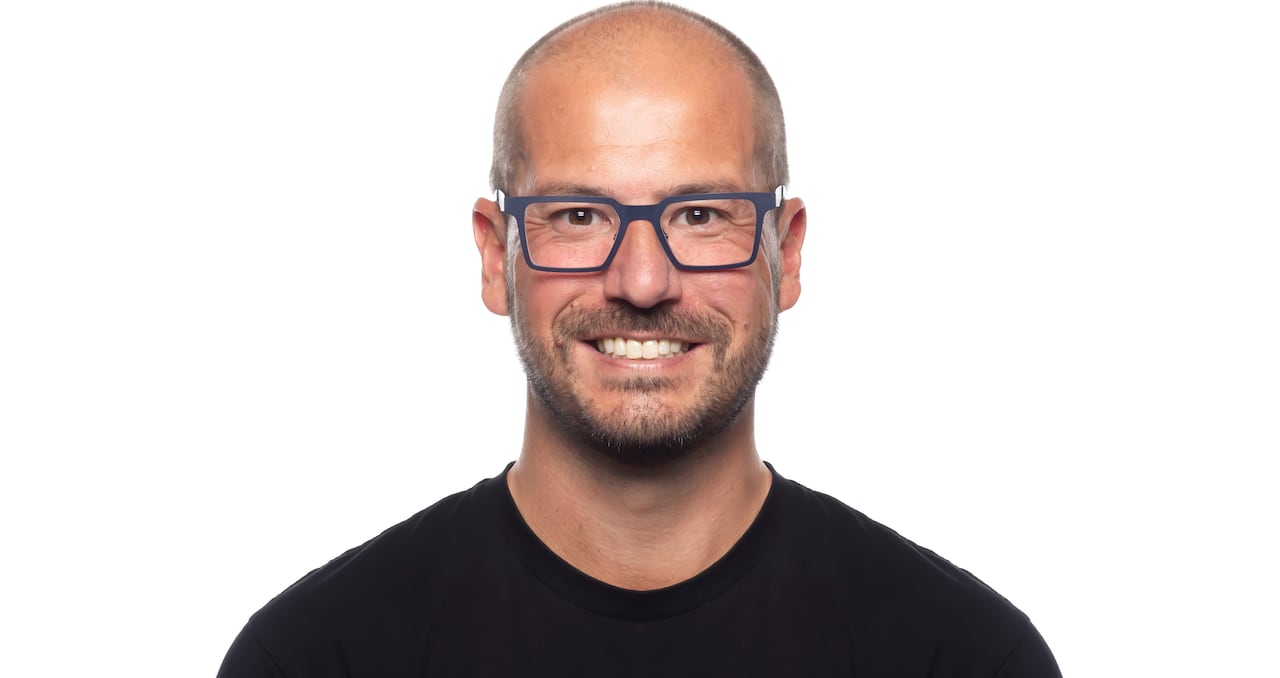 A professional headshot of a man wearing glasses and a black shirt