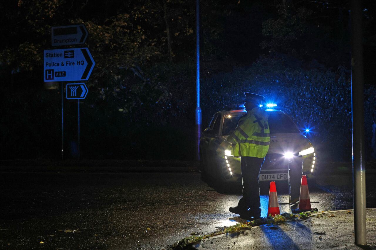 A police officer stands guard next to a vehicle with flashing ilghts.