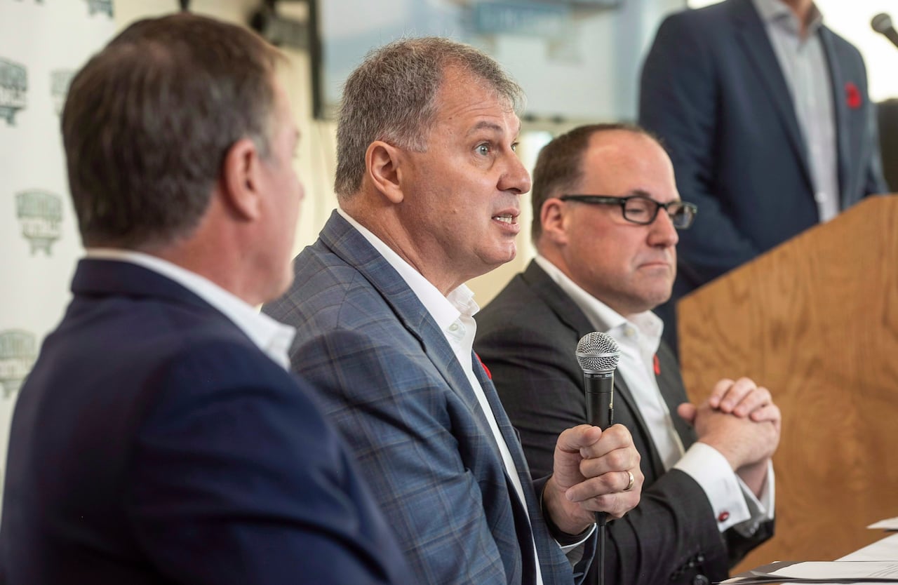 Three men wearing suits are shown at a press conference.