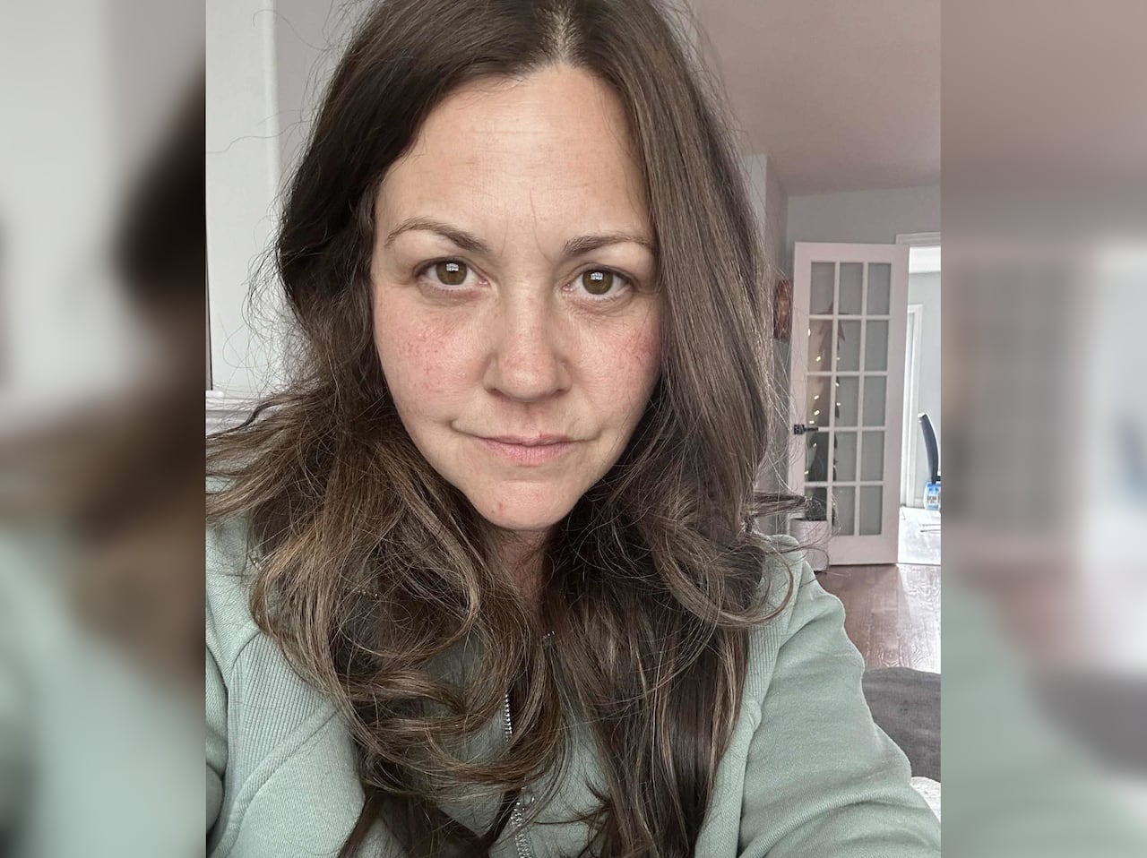 A woman with brown hair and some streaks of grey looks at the camera.