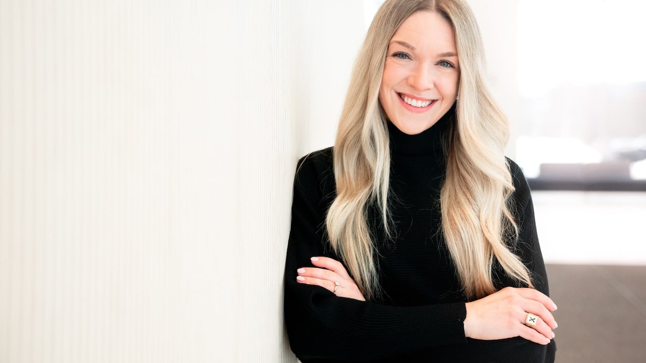 A woman leans against a wall and smiles.
