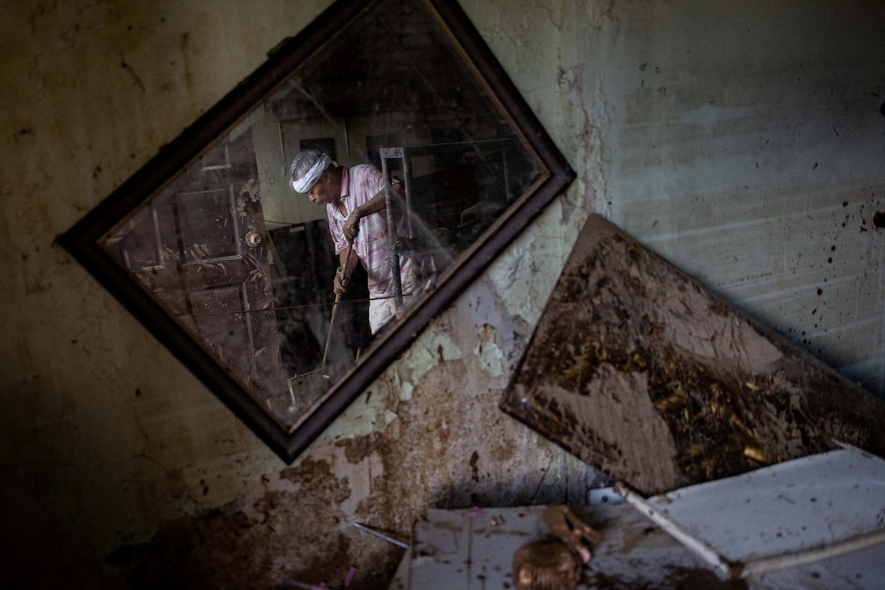 A person sweeping a room damaged by a typhoon; his reflection is seen in a crooked mirror.