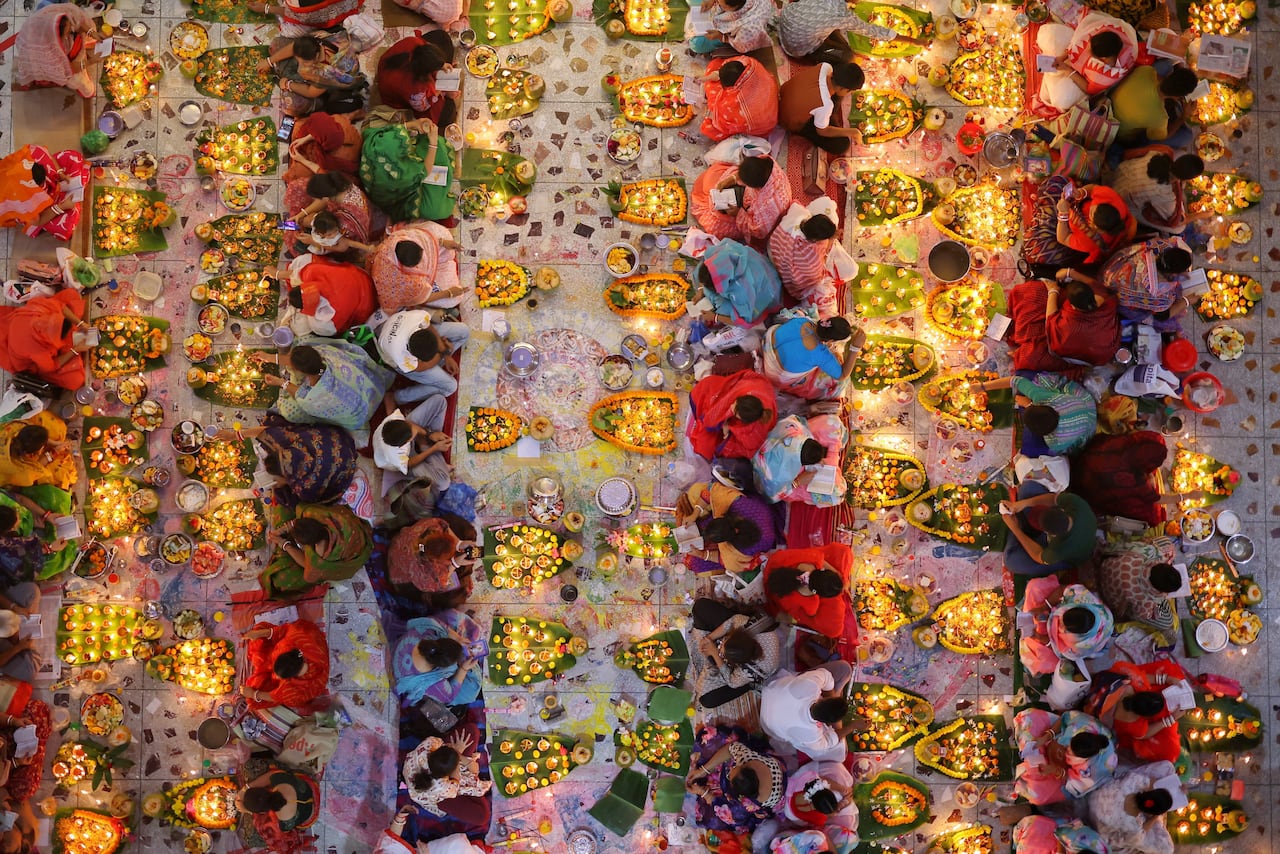 A bird's-eye view of people sitting on the ground with their backs to one another with votives laid in groups in front of each person.