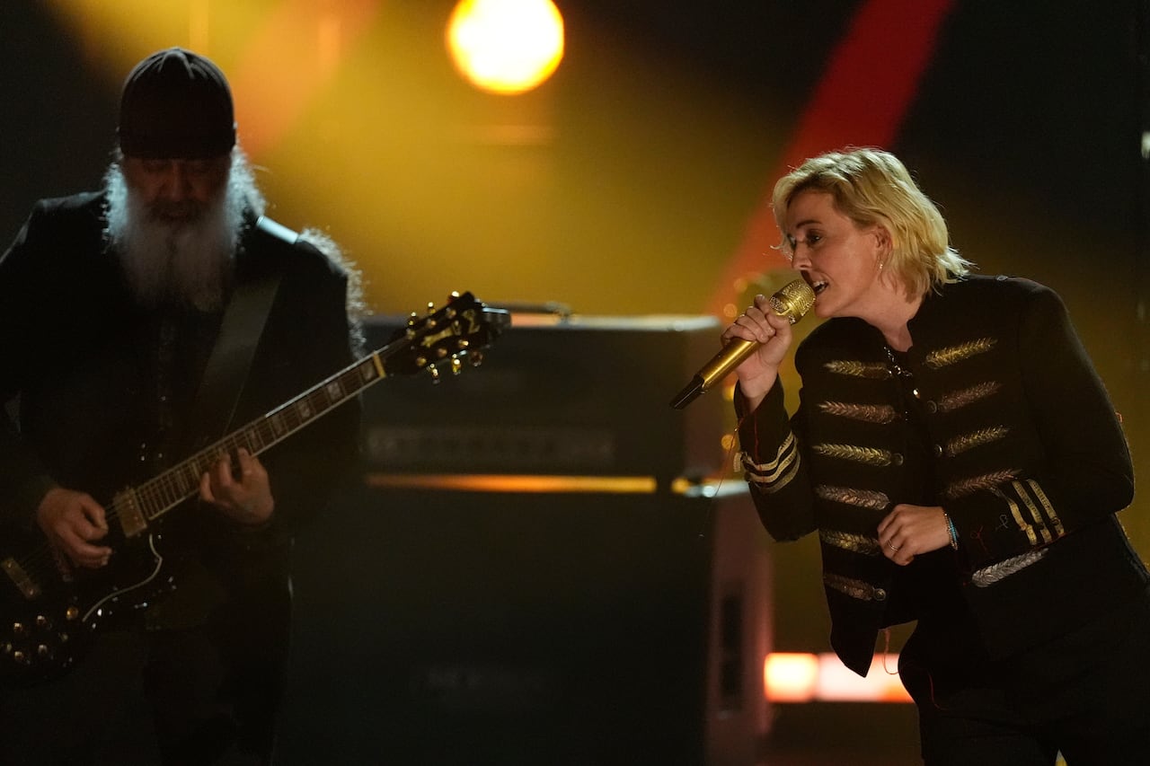 A man on the left plays guitar while a woman on the right leans toward him and sings into a microphone