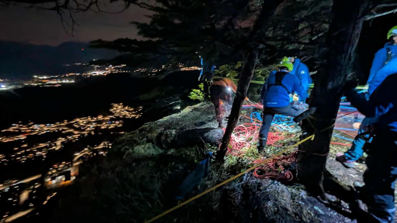 Search and rescue teams stand on the right side with a mountain cliff to the left