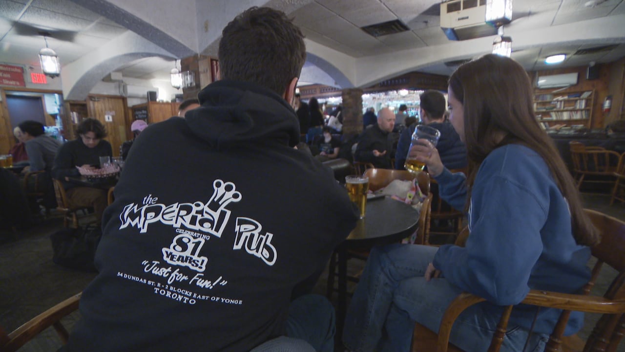 Two patrons sit at a table nursing beers at the Imperial Pub on it's last day open. One wears a hoodie with the pub's logo on it.