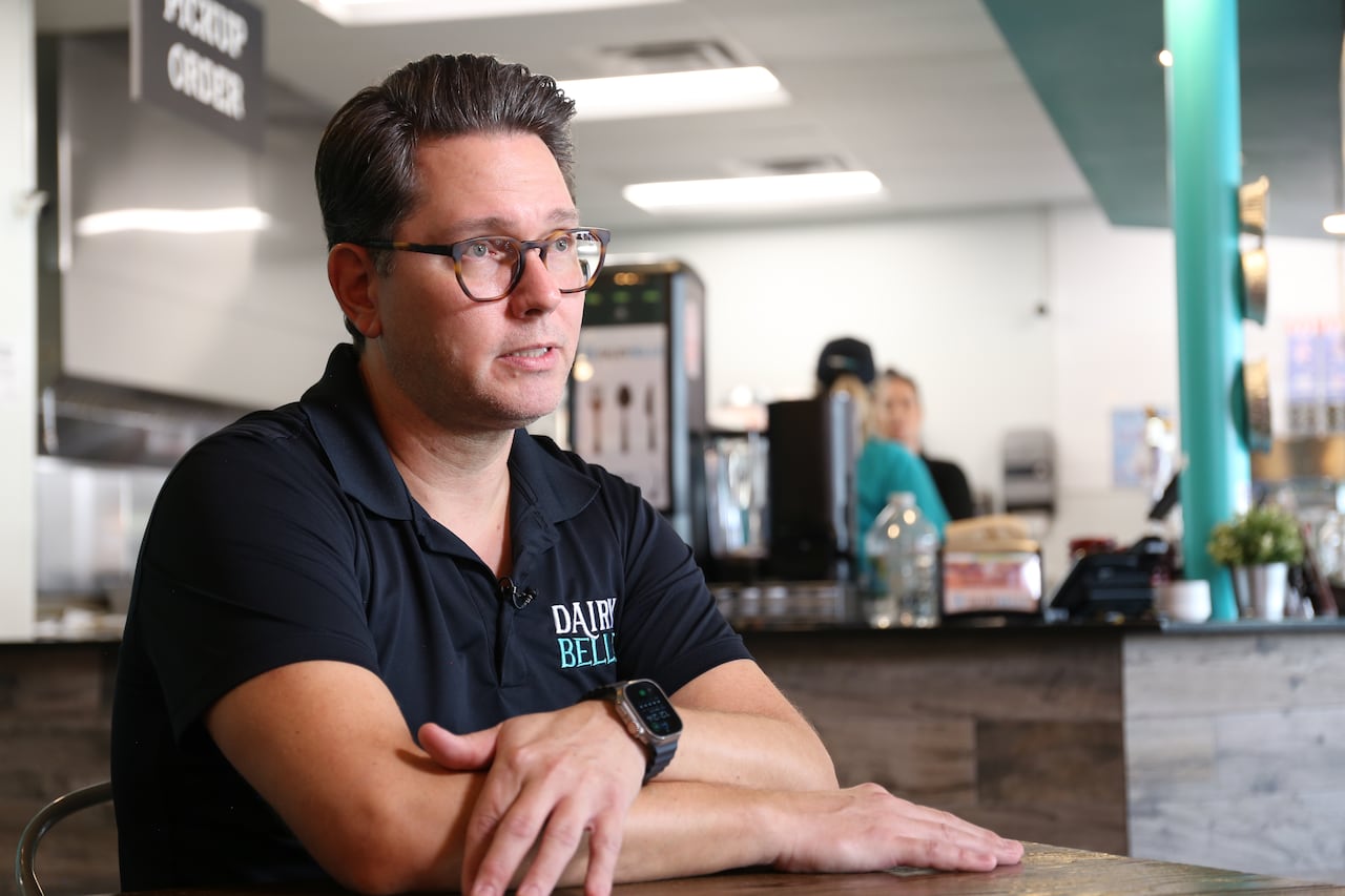 A man in a black polo shirt sits at a table in a restaurant.