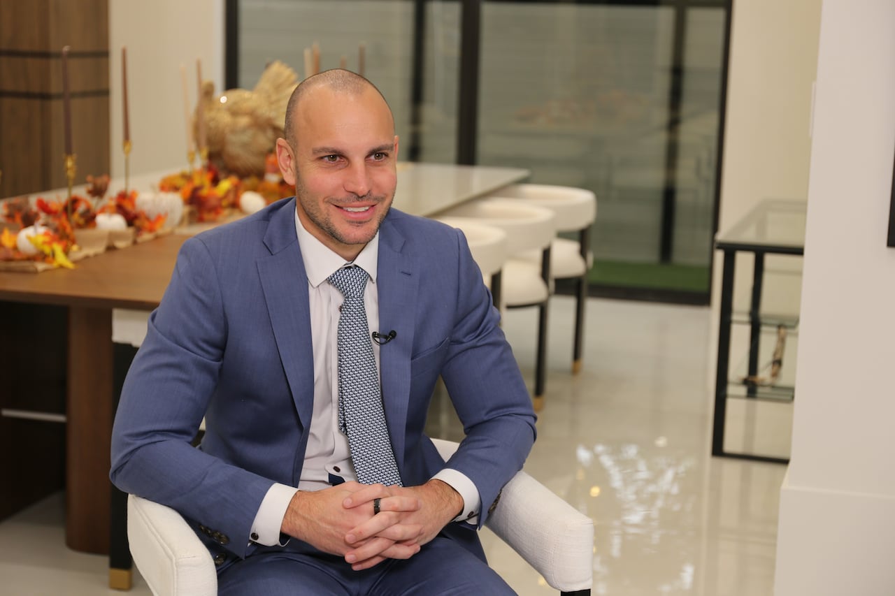 A man in a blue suit sits beside a long table.