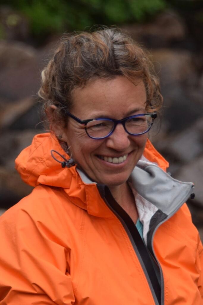 A woman in a bright orange jacket smiles to someone off camera