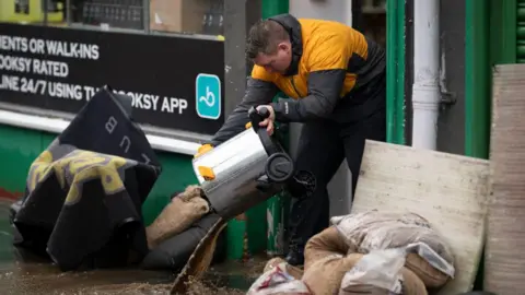 Getty Images A man in a yellow and grey anorak bails water out of a business in Pontypridd. The water is coming over the doorstep.