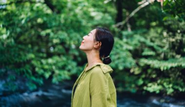 Woman in green blouse standing in nature with eyes closed smiling