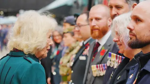 Reuters Queen Camilla, wearing a jade green jacket, speaking to armed service personnel