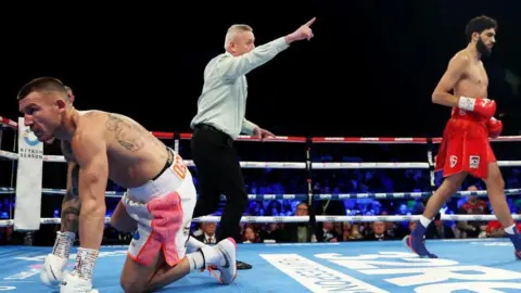 Getty Images A man on all fours in a boxing ring while the referee waves his opponent away.