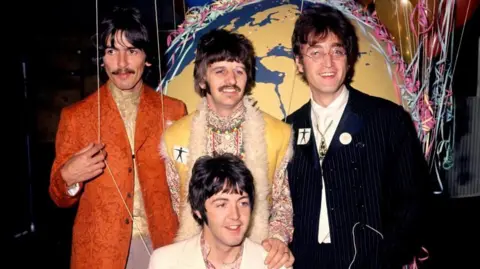 PA Media The four members of the Beatles - George Harrison, Ringo Starr and John Lennon stand side by side, and Paul McCartney crouches down in front of them. Ringo has his hand on Paul's shoulder. There are balloons and streamers in the background