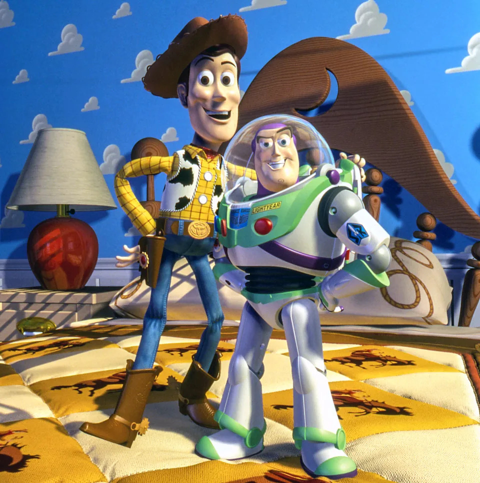 Woody, a cowboy doll, and Buzz Lightyear, a space ranger toy, stand confidently on a bed in a child's room with cloud wallpaper