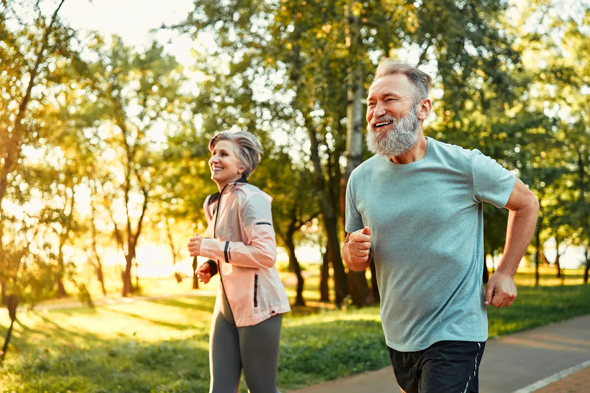 Senior woman and man running through forest