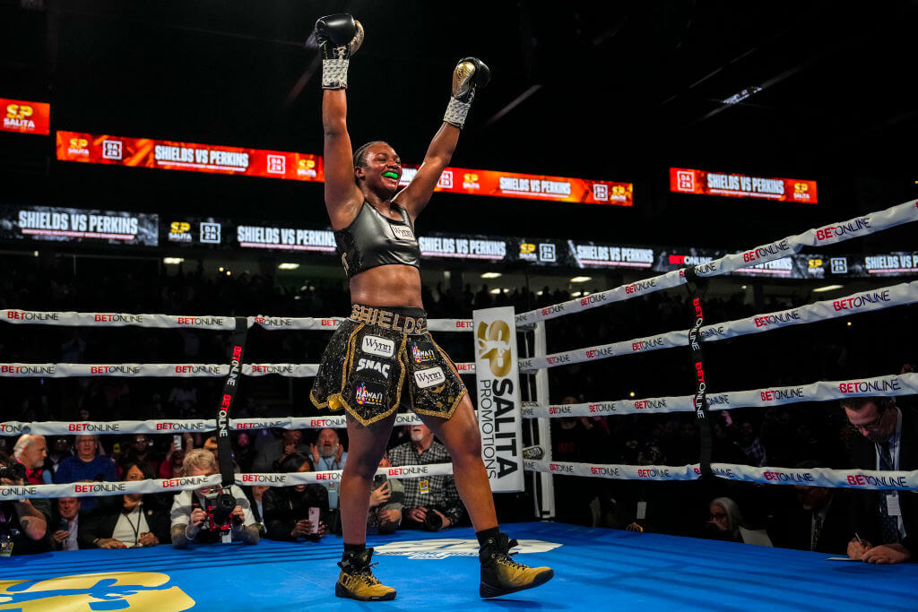 Claressa Shields raising her arms in victory inside a boxing ring.