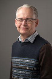 A man with white hair and glasses smiling for the camera.
