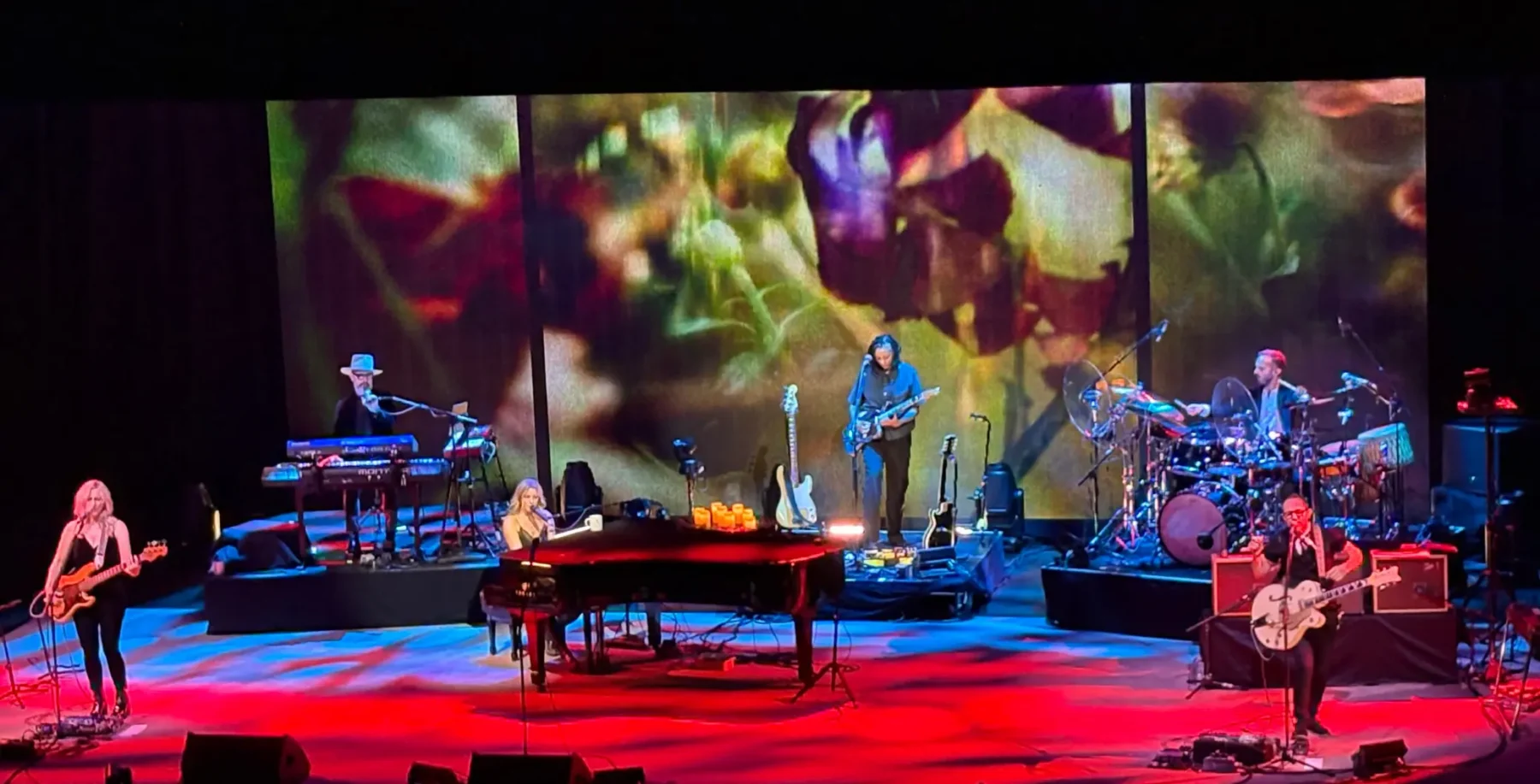 Colorful live music performance on stage with band members playing guitars, keyboard, drums, and vocals against a vibrant floral background, showcasing Toronto's music and arts scene.
