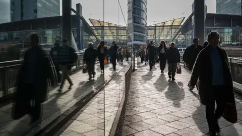 Getty Images Commuters walking in shadow next to a glass building.