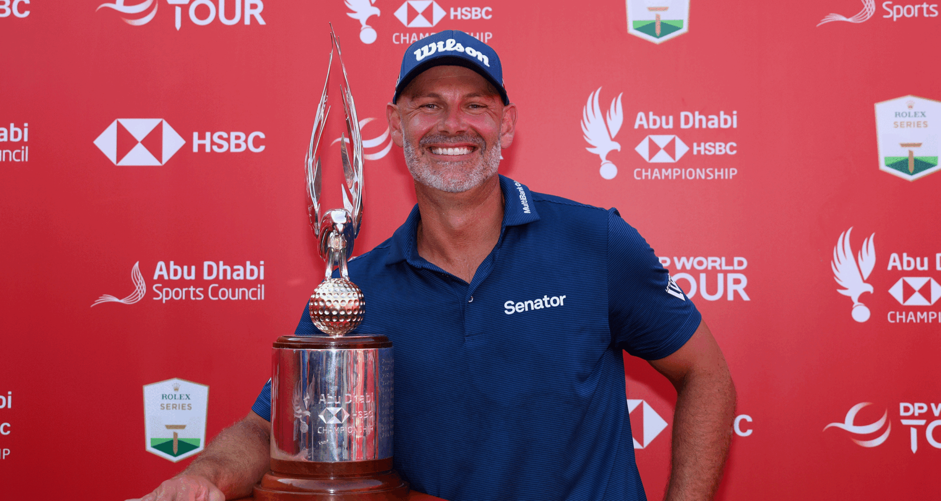 Paul Waring smiles while posing next to the Abu Dhabi HSBC Championship trophy