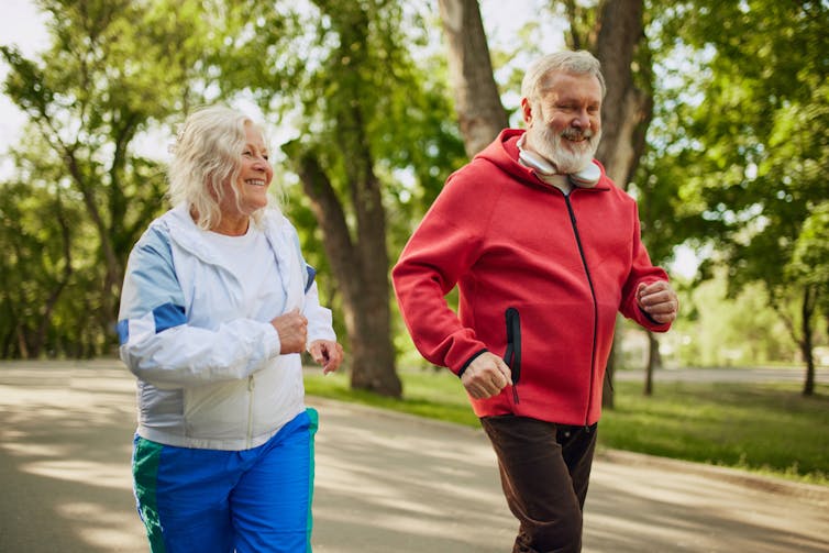 An older woman and man go for a run in a park.