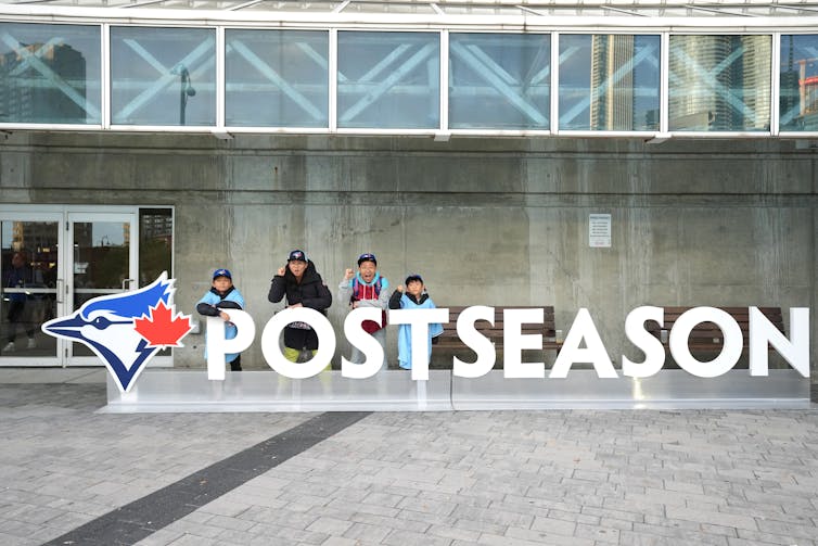 People pose with a sign that says 'postseason' beside the Toronto Blue Jays logo