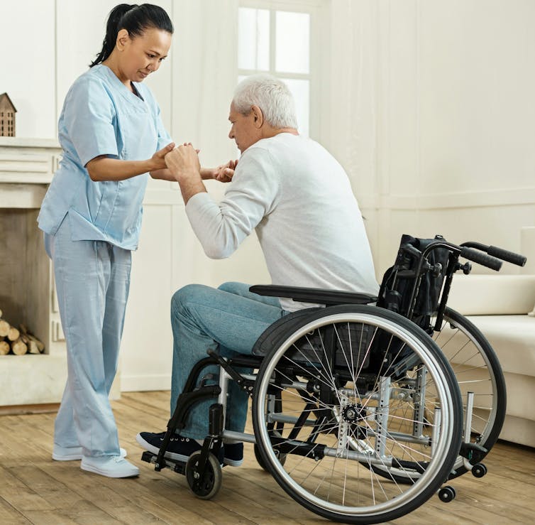 A woman helping a man in a wheelchair.