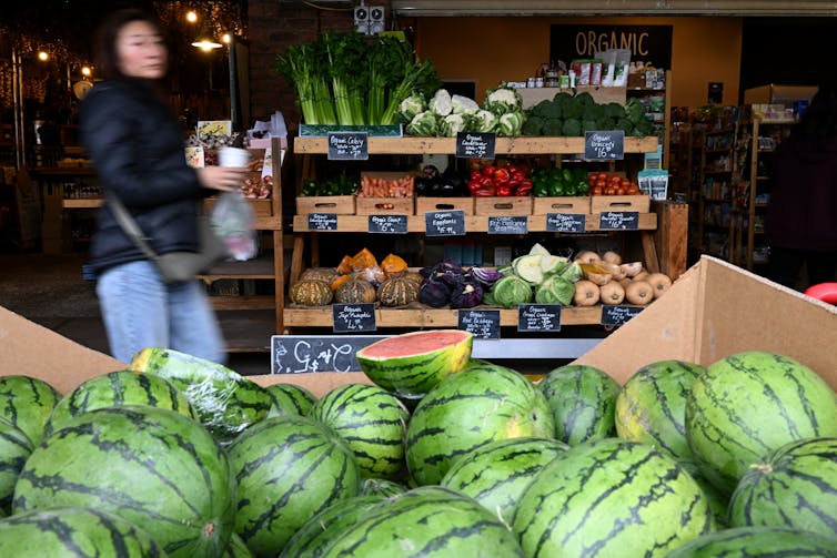 A fruit and vegetable market, featuring a large box of watermelons.