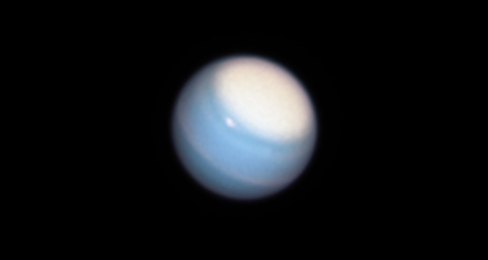 The ice giant Uranus is pictured shining against the blackness of space. Its blue surface is marked by lighter clouds and an equatorial band, while a large pale cloud hovers over its polar region.