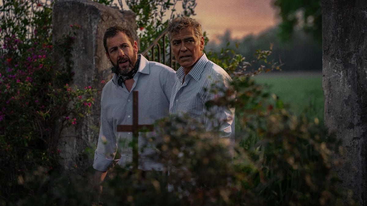 a movie still of Adam Sandler and George Clooney standing in what appears to be a park or forest