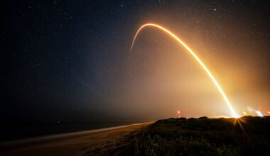 a time-lapse photo showing a streak from a rocket launch arcing over the beach at night.