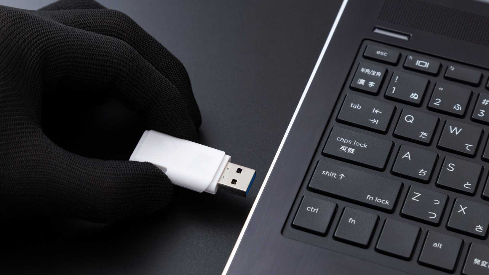 A gloved hand inserts a USB drive into a laptop.